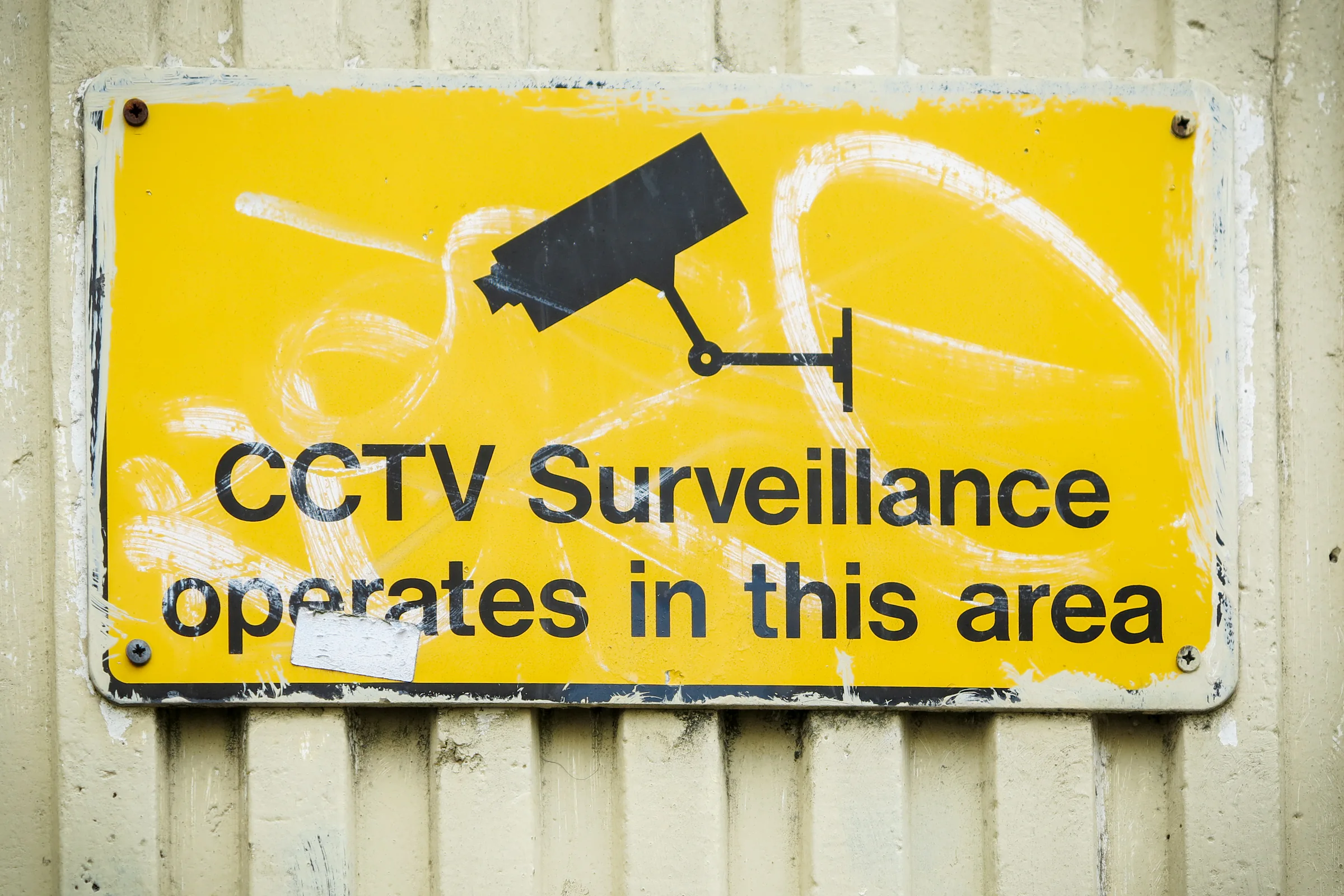 Weathered yellow CCTV surveillance sign